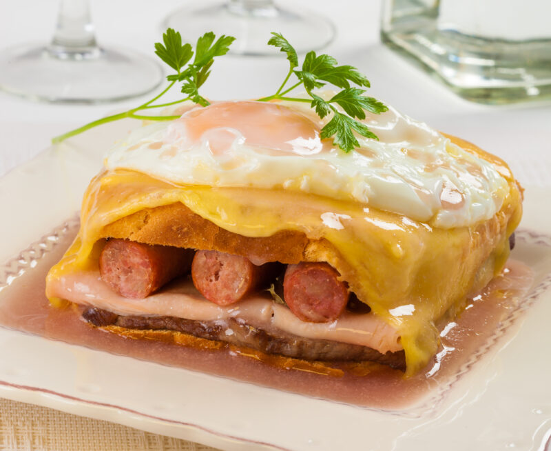 A large sandwich with three sausages, ham and an egg on top.