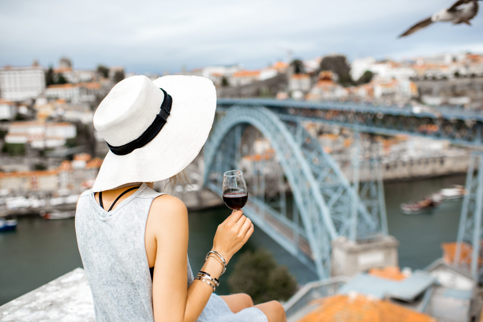 Woman in hat drinks wine by a bridge